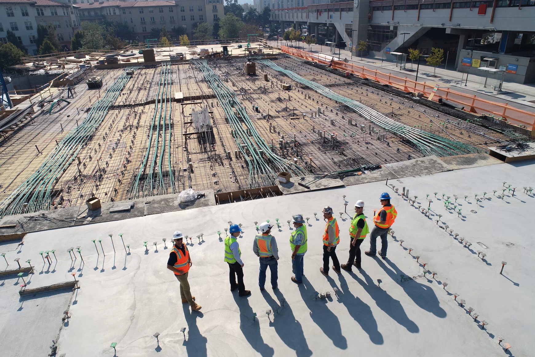 Construction site with workers in safety gear on a concrete slab overlooking rebar and utilities